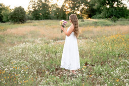 young woman with long hair stands in a field of wildflowers and holds a bouquet