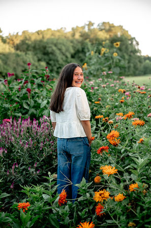 teenage girl stands in a flower garden and smiles over her shoulder