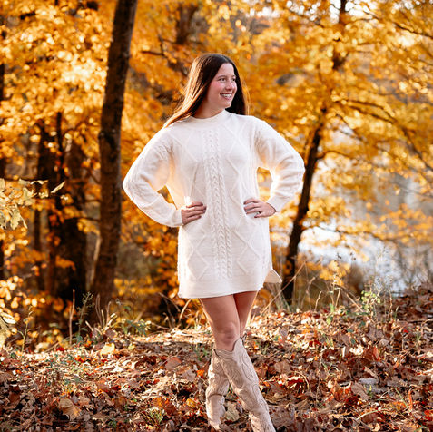 senior girl stands in cream dress and boots with fall leaves around her