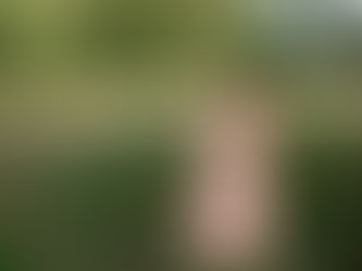 Senior girl smiles in a grassy field in a long floral dress, sunlight streams in behind her