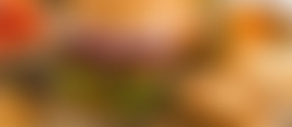 Juicy cheeseburger with bacon, lettuce, and onion on a sesame bun, surrounded by crispy chips. Rustic wood table, fresh tomatoes nearby.