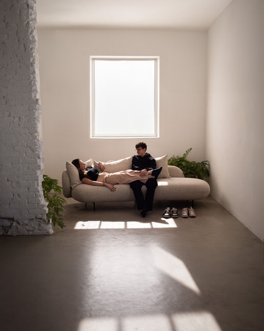 Couple sitting and lying on the Maison Sofa in a bright room with a white brick column