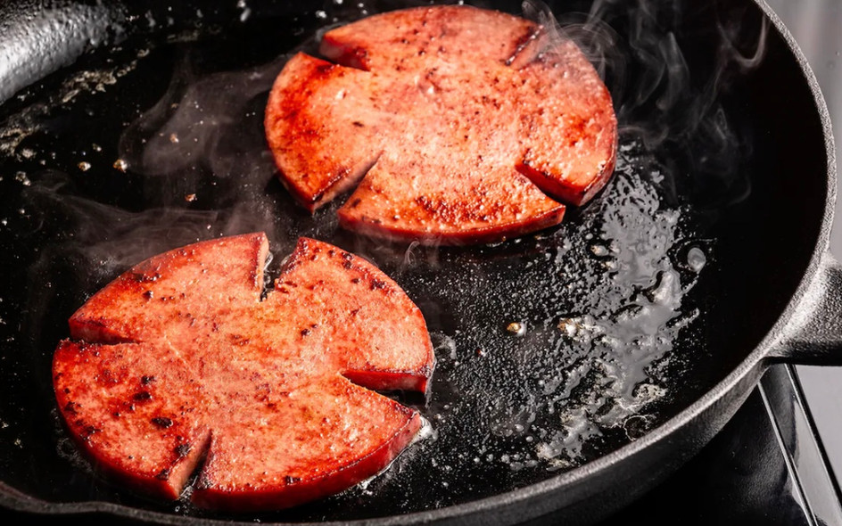 Two slices of bologna frying in a cast iron skillet