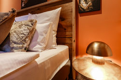 Nahaufnahme vom Bett vor einer einladenden roten Wand mit goldenem Nachttisch