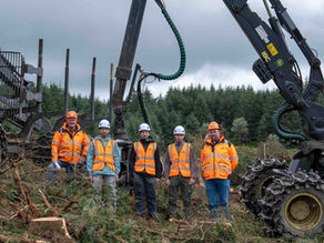 Dean Close School students and SDL Solutions staff standing together on a forestry site, wearing high-vis PPE, with forestry machinery and woodland in the background.