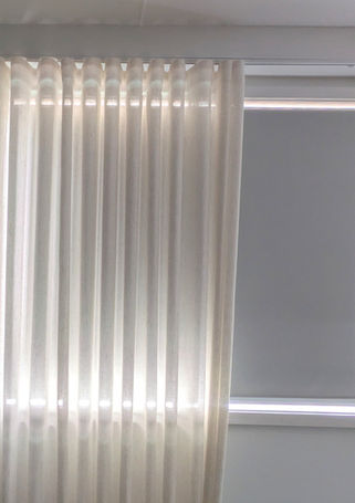 Sunlight streams through sheer white curtains covering a window blind.