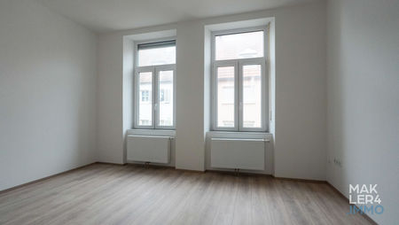 Helles Schlafzimmer mit zwei großen Fenstern, modernem Boden in Holzoptik und hohen Decken.