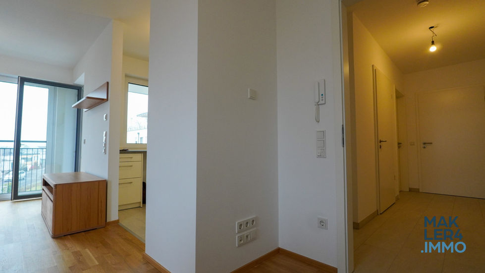 Offene Wohnküche mit Blick in den Flur. Eine große Glas-Balkontür sorgt für viel Tageslicht. Die Küche ist in hellen Tönen gehalten und verfügt über moderne Einbaugeräte.