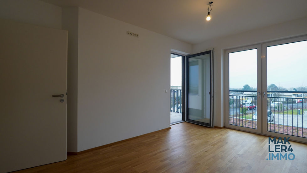 Schlafzimmer mit großen Fenstern und direktem Balkonzugang. Der helle Holzfußboden harmoniert mit den weißen Wänden