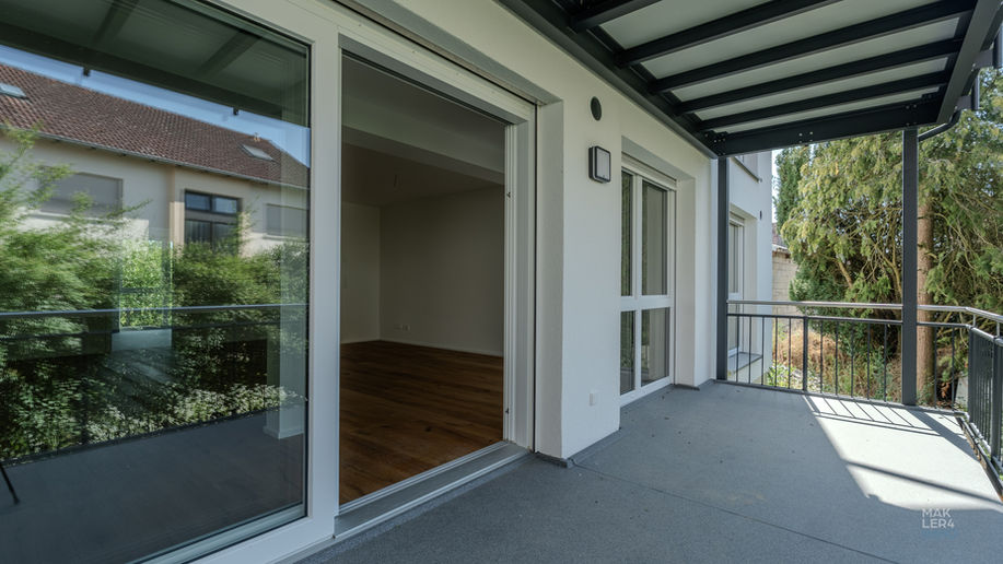 Überdachter Balkon mit Glasfront, Geländer und Blick ins Grüne
