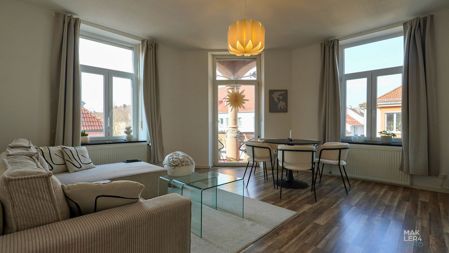 Heller Wohnbereich mit Sofa, großen Fenstern und Zugang zum Balkon