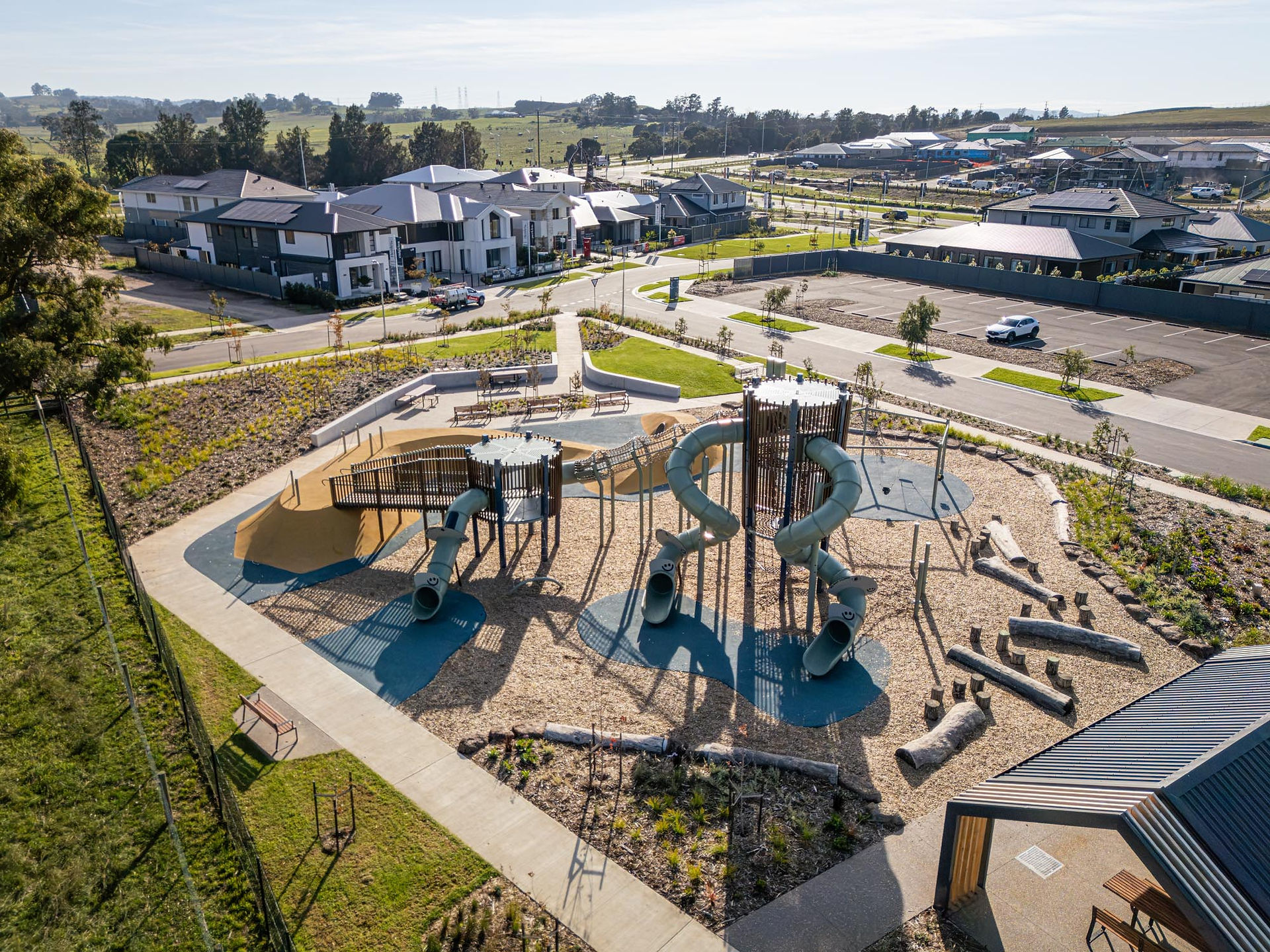A multi-level custom timber look playground featuring two large towers linked by a suspended rope mesh tunnel, multiple tube slides, an internal rope climbing net and an elevated bridge.