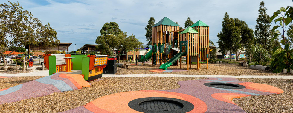 A vibrant outdoor playground featuring a large timber-look giant treehouse system with slides, inclusive play areas like the Smooth Glider, built-in ground trampolines and a sand play pit.