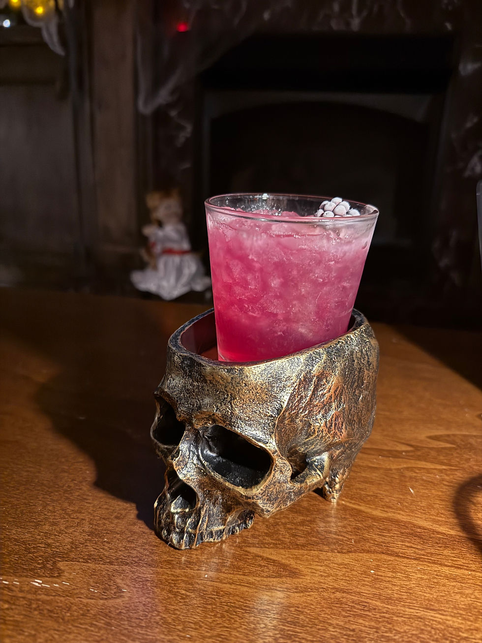 A pink cocktail with purple freeze dried garnish inside of a skull cup in a speakeasy