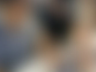 Two people focused on solving a blue jigsaw puzzle at a table. The setting is indoors with other people in the background.