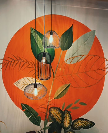 Botanical wall mural with orange circle, leafy artwork, and hanging lights