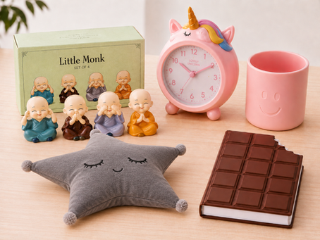 Office decor items from The QWERTY Store featuring mini monk figurines, a unicorn clock, pink organizer, dark star cushion, and chocolate-style notebook.