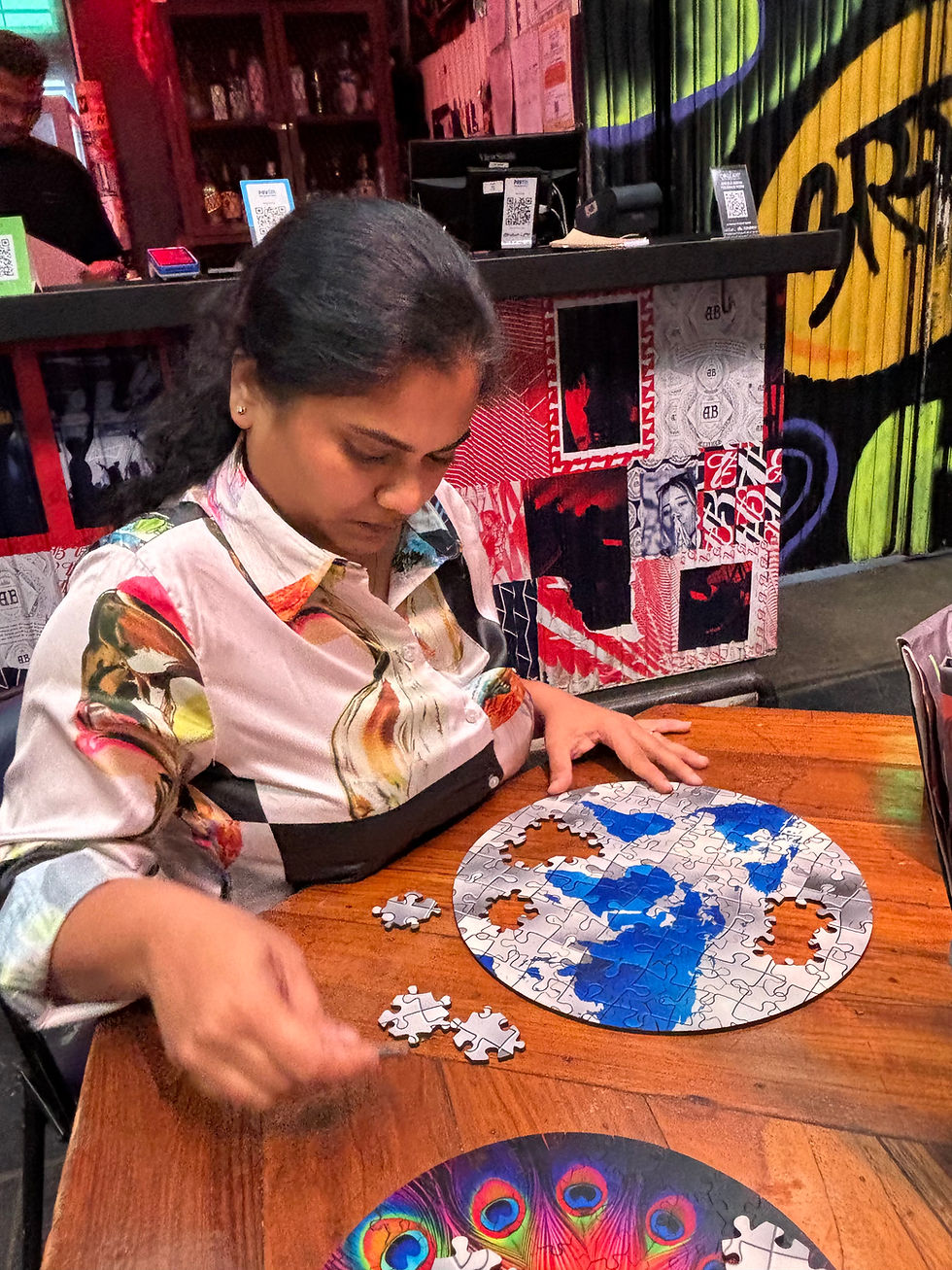 Woman in a patterned shirt assembles a round jigsaw puzzle at a wooden table in a colorful café with QR code signs.
