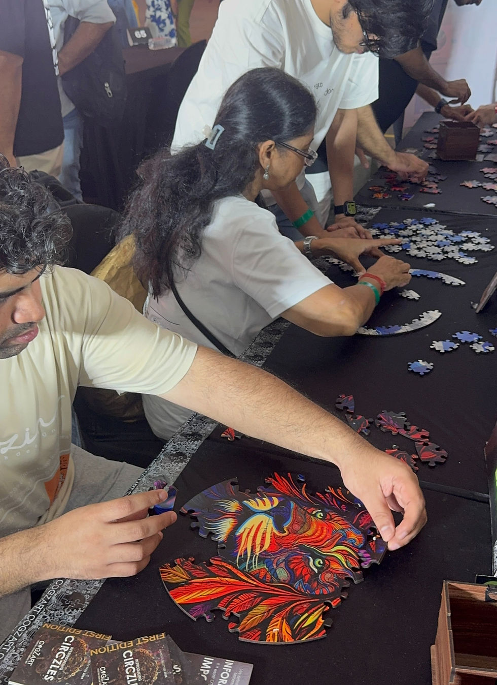 People assemble a colorful puzzle featuring a vivid animal design on a black table. Brochures are visible, creating a focused atmosphere.