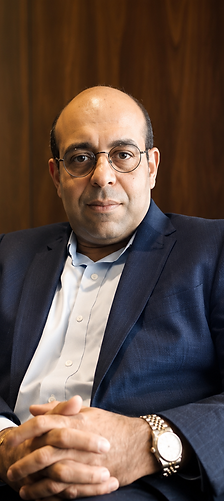 Senior business leader seated in a navy blazer and glasses during a professional portrait session.
