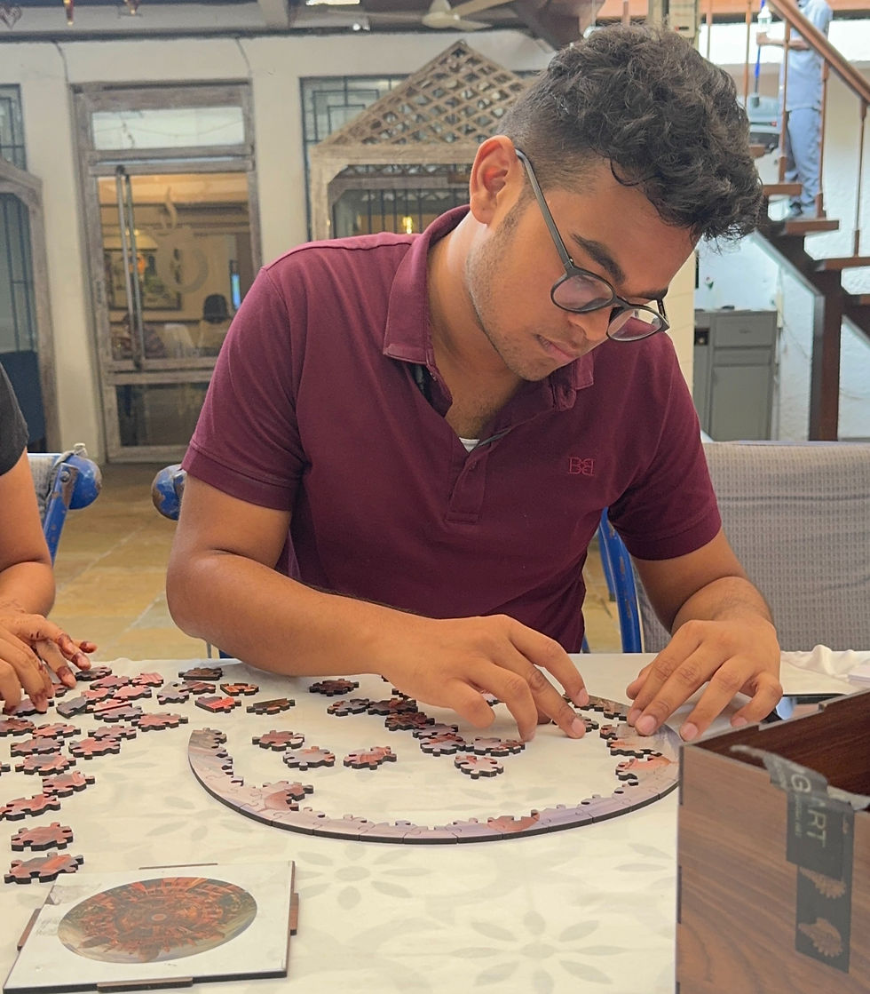 Man in a maroon shirt focused on assembling a round puzzle at a table. Interior setting with decorative wooden elements in the background.