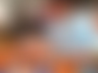 A man in a blue T-shirt happily assembles a circular puzzle on a wooden table in a cafe. Others sit in the blurred background.