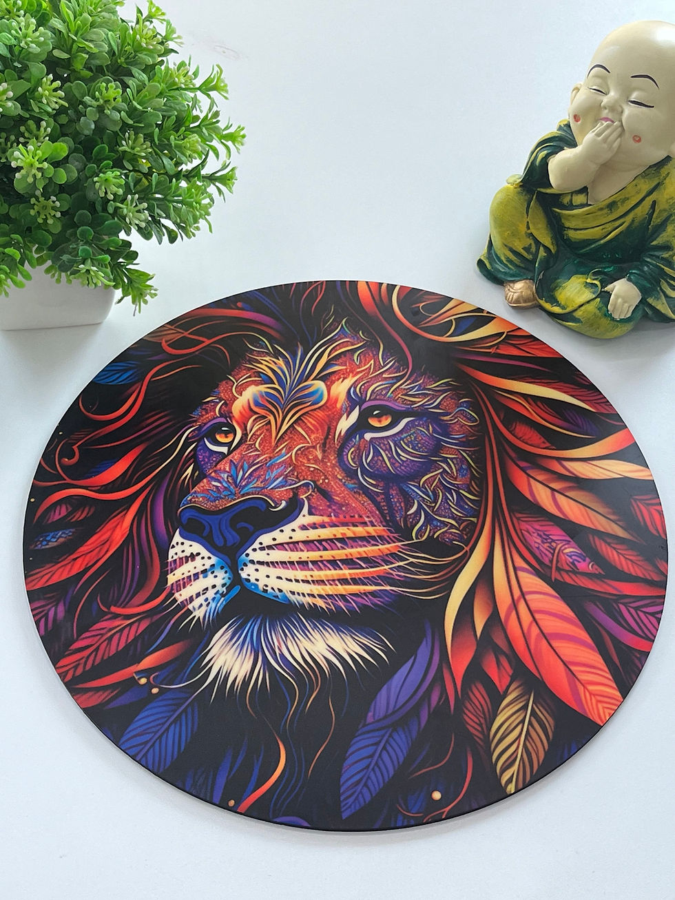 Vibrant lion artwork with colorful patterns, beside a smiling Buddha statue and green plant on a white surface.