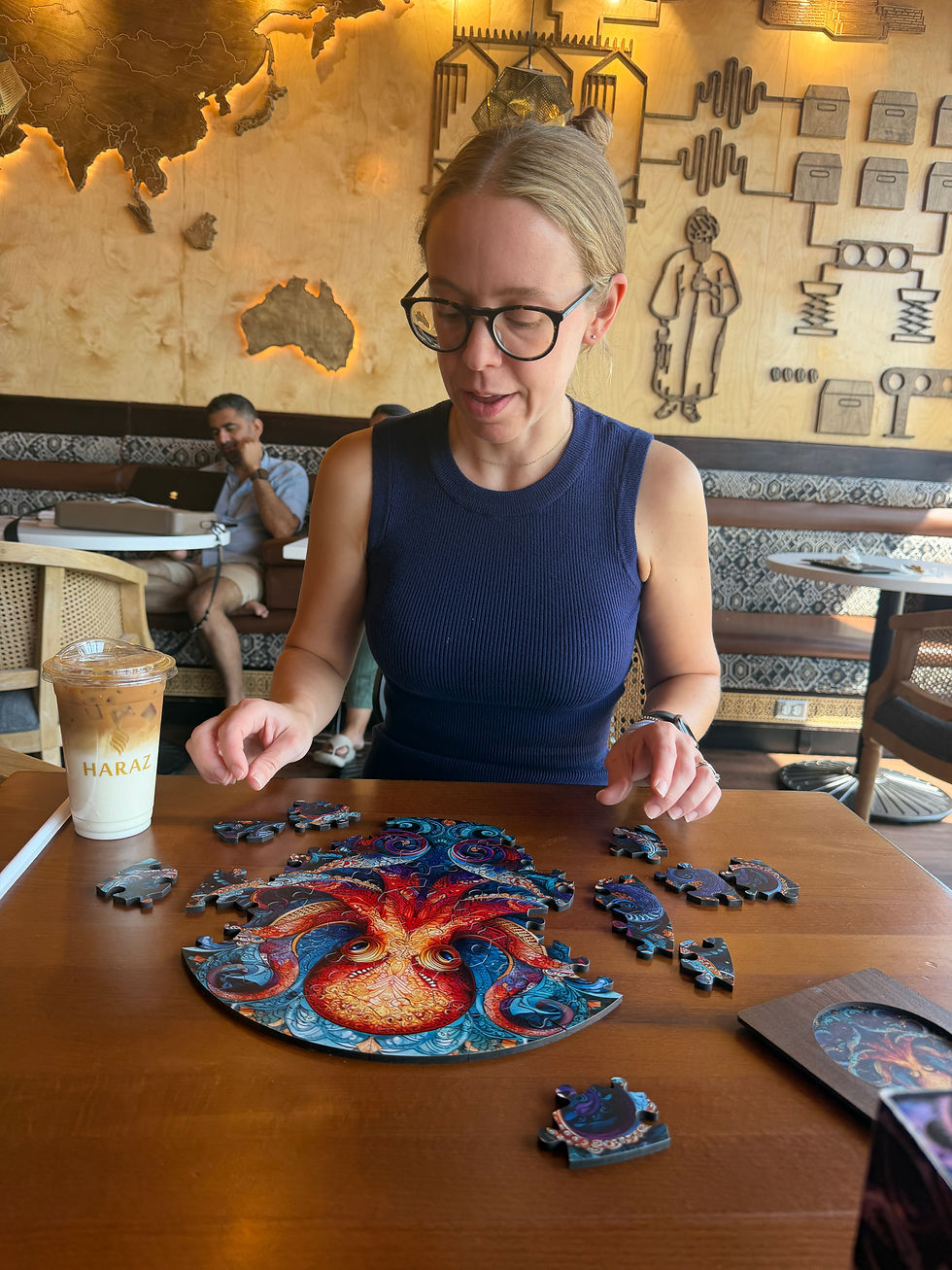 A woman assembling a colourful octopus-themed Adult Jigsaw puzzle at a café, showcasing Cognitive Activities for Adults.