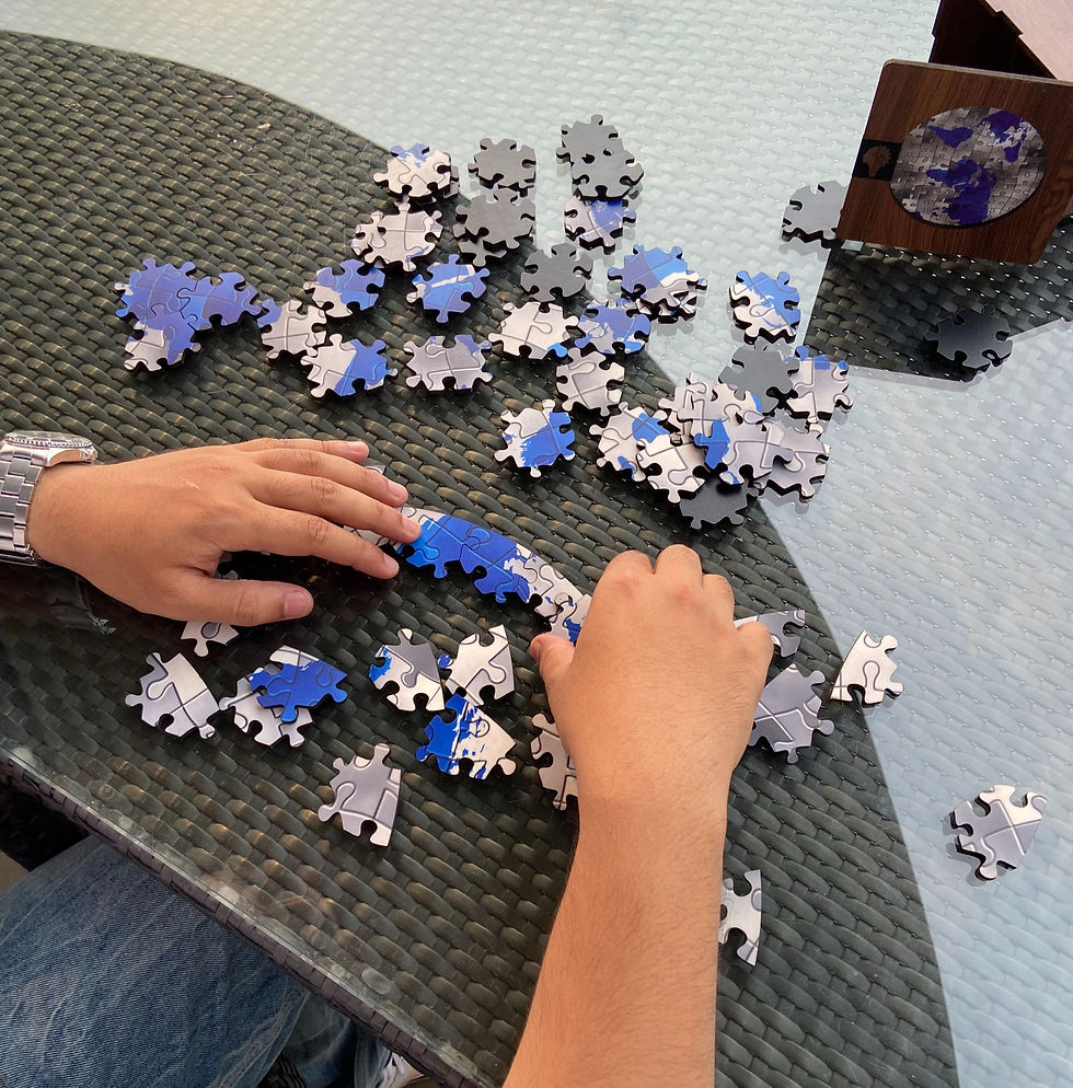 Hands assembling a blue and gray puzzle on a glass table, with a wooden box nearby. The mood is focused and calm.