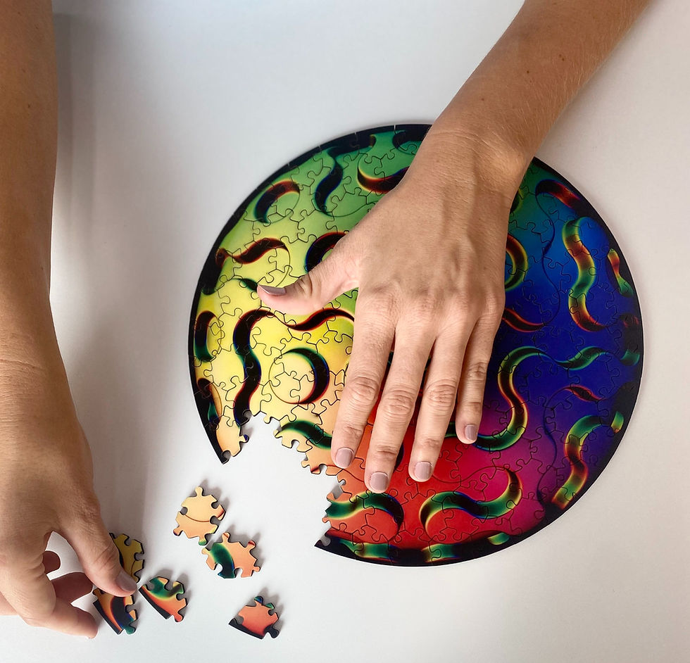 Hands assembling a colorful circular puzzle with swirling patterns on a white surface.