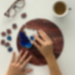 Hands assembling a round wooden puzzle with a blue butterfly. Glasses and coffee cup nearby on a white surface. Calm, focused mood.