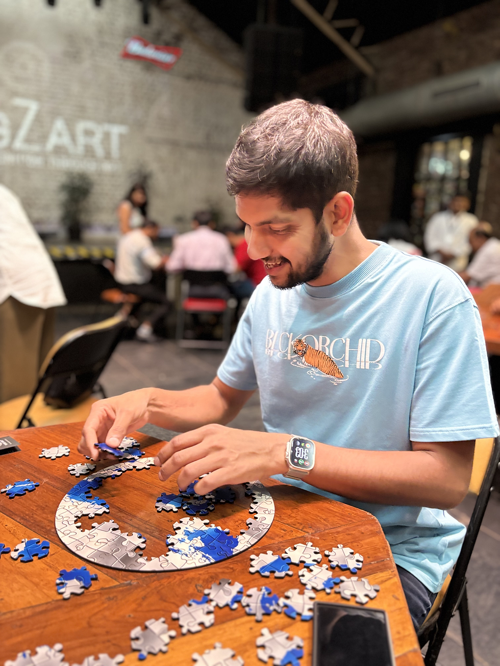 CogZart puzzle event participant solving a circular jigsaw at a wooden table, with blue and white pieces spread around in a lively indoor venue.