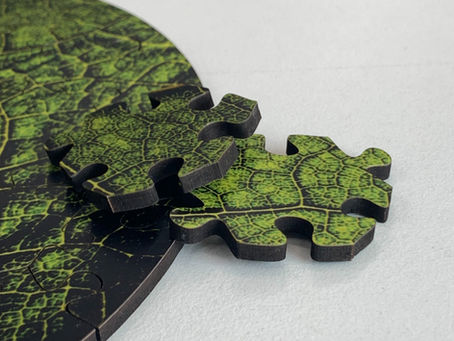 Close-up of green, leaf-patterned puzzle pieces partially assembled on a light surface. Two pieces are prominently displayed.