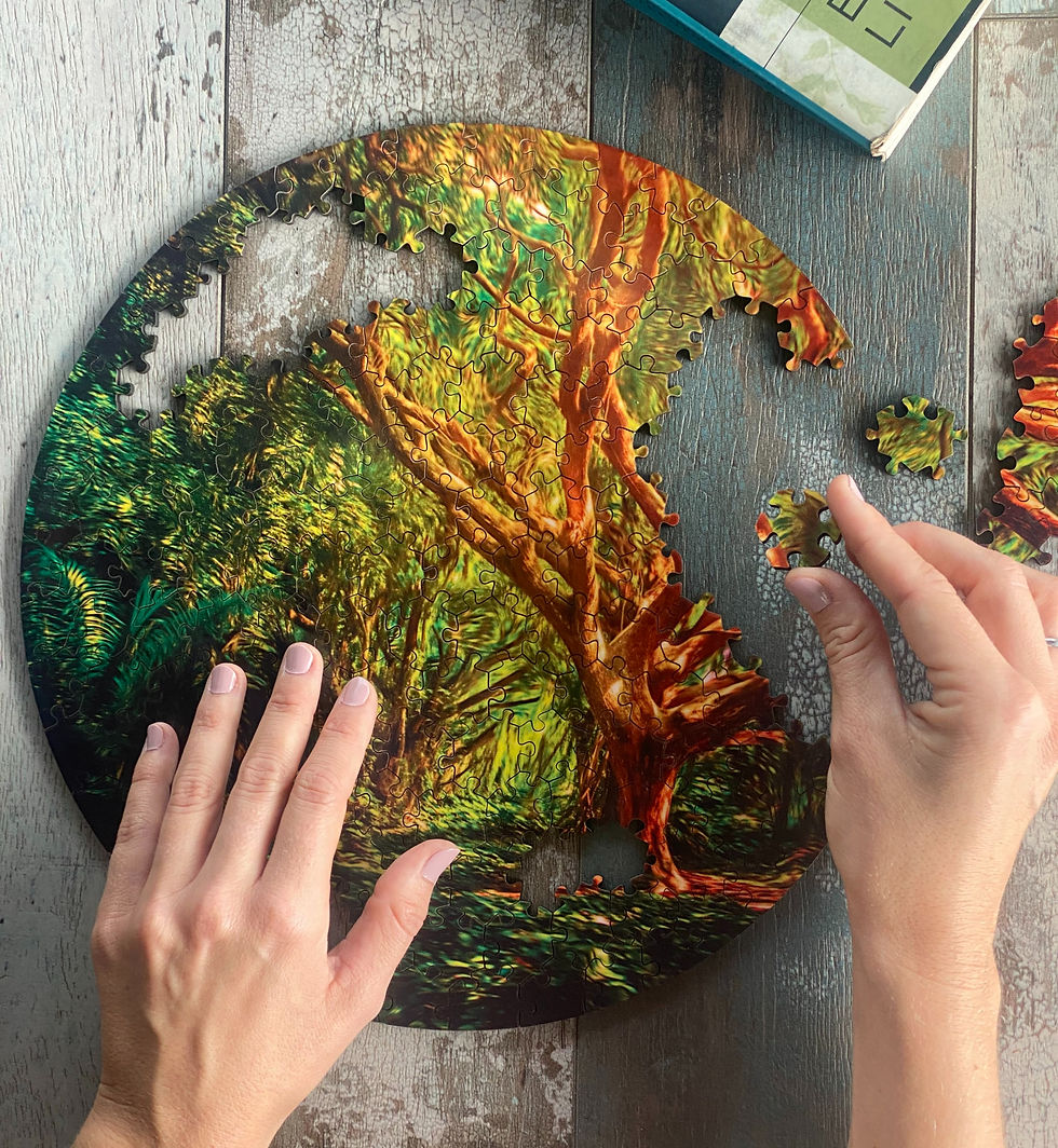 Hands assembling a vibrant, round puzzle of a tree with green and orange hues on a wooden table. Box with text partially visible.