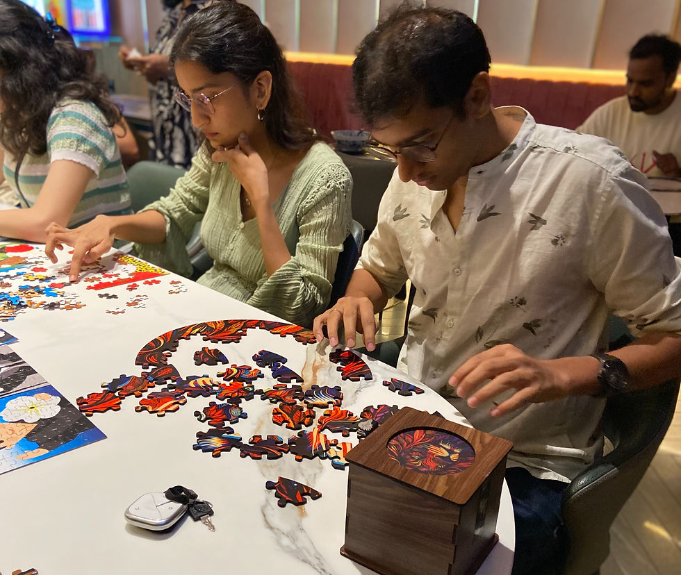 People solving a colorful jigsaw puzzle at a table in a warm-lit room, focused and quiet; pieces scattered beside a wood box and keys.