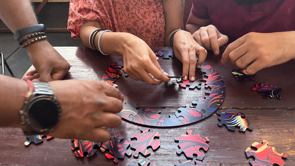 Hands assembling a colorful jigsaw puzzle on a wooden table. Three people engage in the activity, showing focus and teamwork.