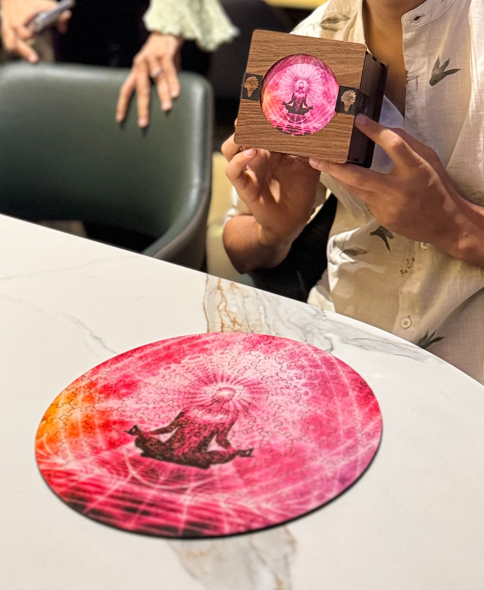 Person holds a wooden box showing pink circular meditation art; a matching round puzzle lies on a marble table.