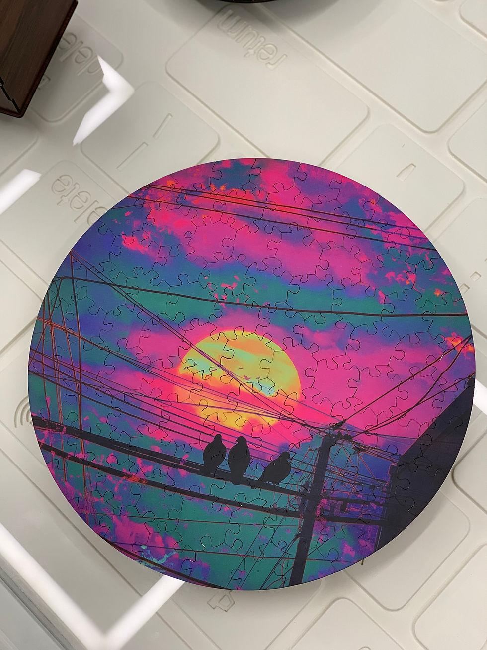 A round puzzle shows a colorful sunset with silhouettes of birds on wires against a vibrant pink and purple sky.