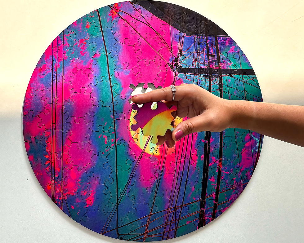 Hand placing the final piece in a vibrant round jigsaw puzzle with pink, blue, and purple patterns. Background is light and neutral.