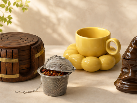 The image shows a curated kitchen decor arrangement featuring a wooden barrel, tea strainer, yellow cup, and ceramic hat-shaped container from The QWERTY Store.