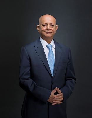 Senior finance executive in a navy suit and blue tie standing against a dark studio background.