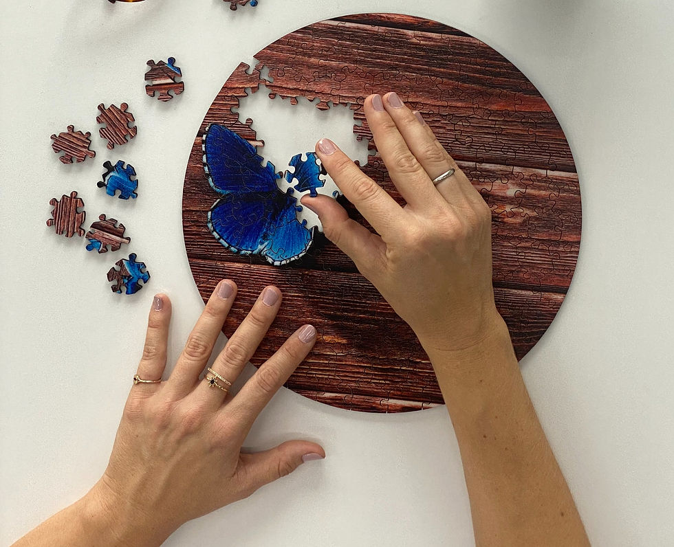 Hands assemble a round wooden puzzle on a white surface, featuring a vibrant blue butterfly. Pieces are scattered nearby.