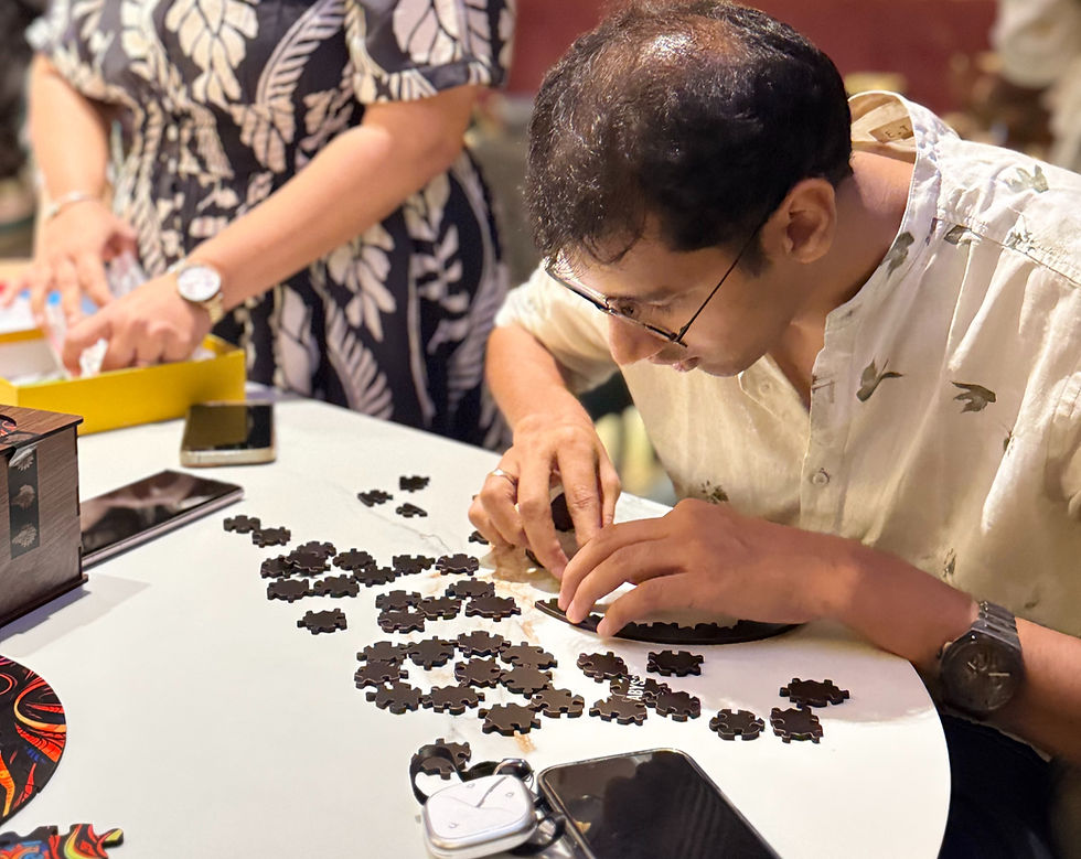 Man in glasses assembles black puzzle pieces at a white table while a woman in a floral dress works beside him.