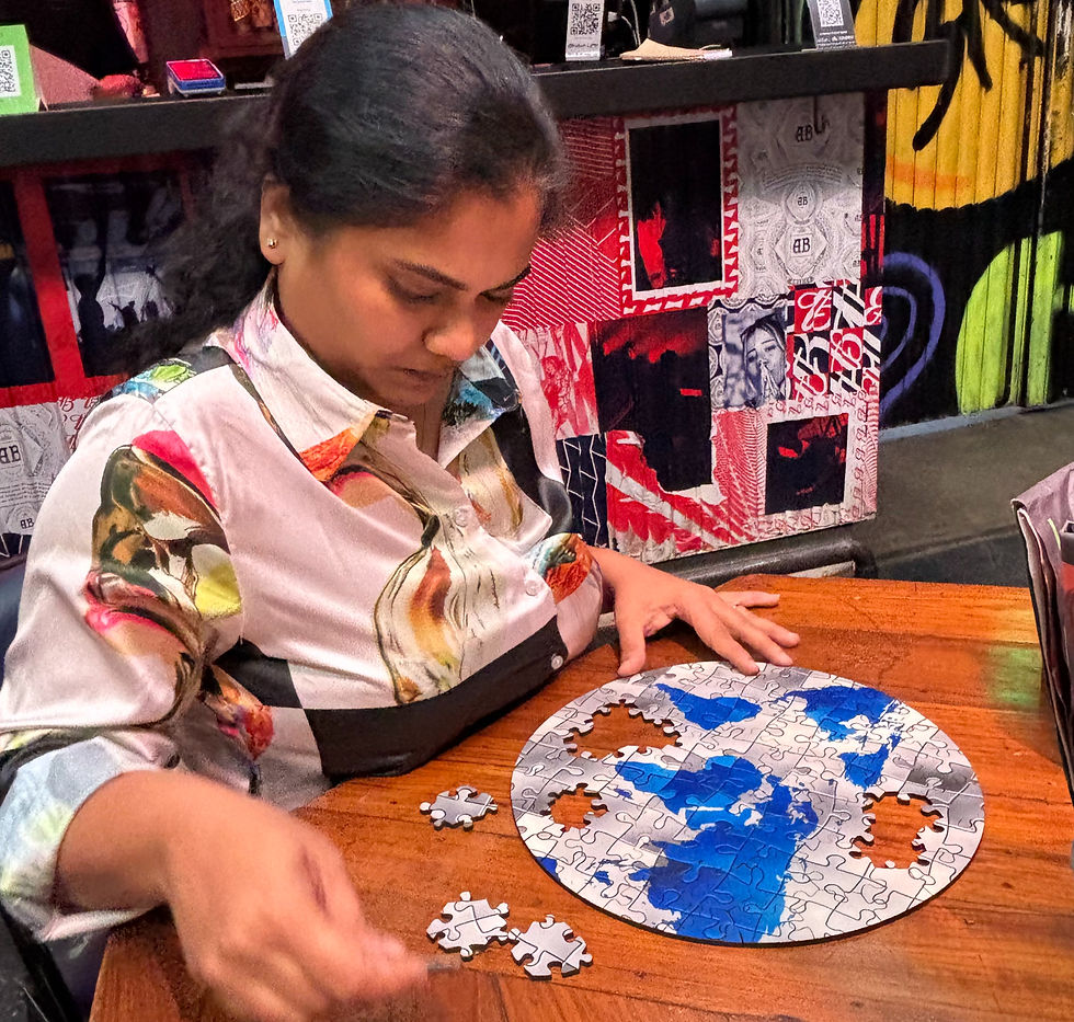 Woman in a colorful shirt studies a nearly completed circular jigsaw puzzle on a wooden table, with pieces scattered nearby.