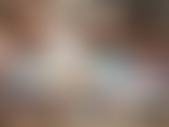 People coloring intricate designs in books on a wooden table. Colored pencils and erasers scattered around. Focused, relaxed atmosphere.