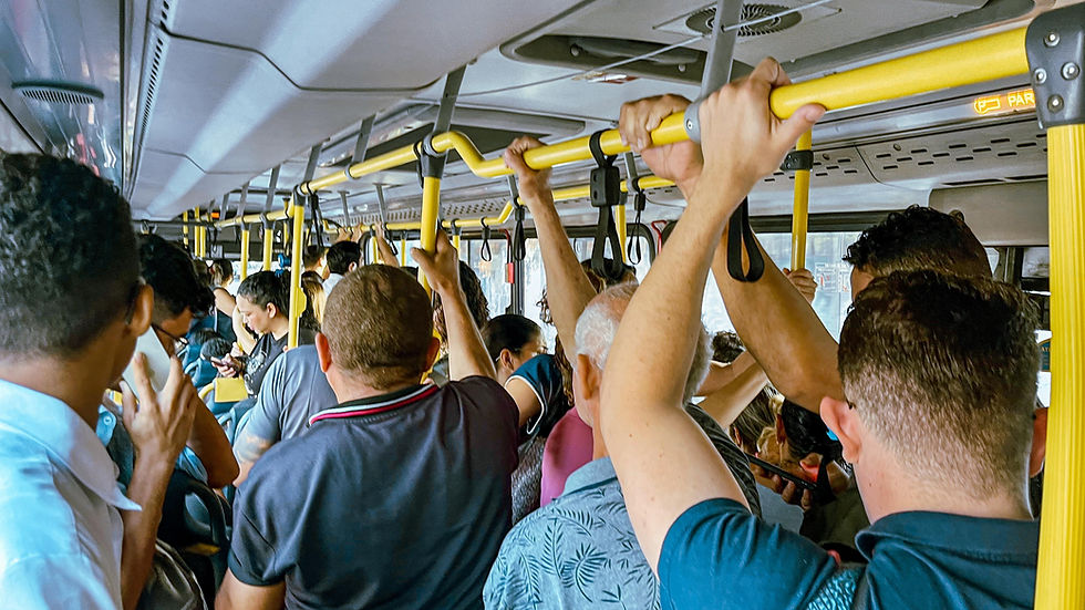 Imagem dentro de um ônibus lotado. Vários passageiros em pé seguram nas barras de proteção do transporte. Todos olham para a frente do ônibus, de costas para a câmera