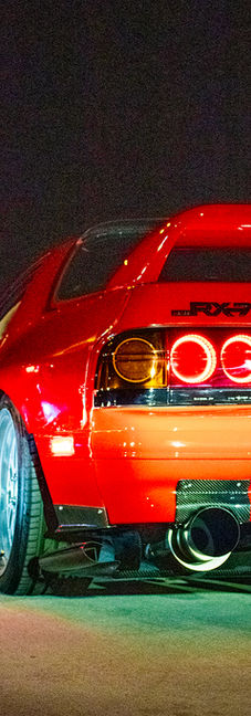 Red car with circular taillights and a large exhaust parked on a parking garage with black sky in background