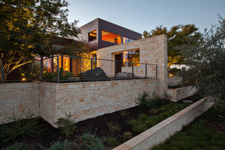 Gold Limestone thin veneer garden walls wrapping a modern hillside home lit at dusk