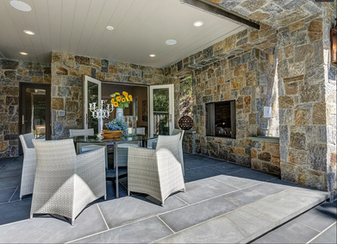 Outdoor dining under a beamed loggia framed by granite veneer walls and a recessed firebox