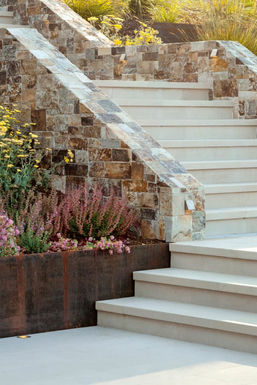 Plaza Buff paving treads beside a stone veneer stair wall and weathered steel planter